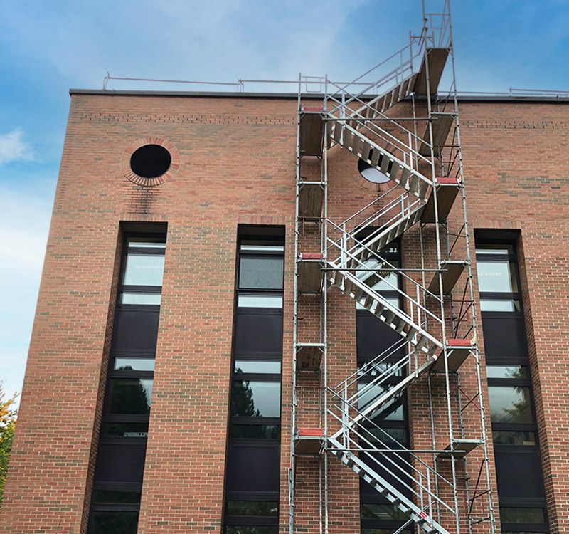 Baugerüst bei einem Mehrparteienhaus mit Passagentunnel und Gerüstverkleidung von Gerüstbau Mair in Tirol